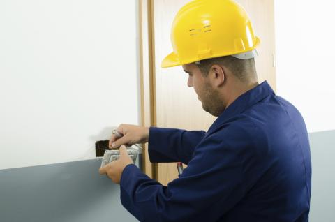 Man with a yellow hat putting a cable into the house wall
